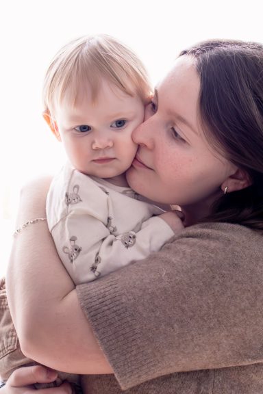 Mamma gosar kärleksfullt med sitt barn framför ett ljust fönster, familjefotografering naturligt ljus, Anna Esmelöv