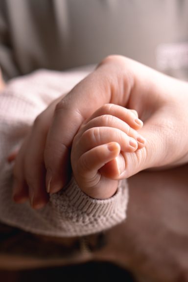 Detaljbild av liten bebishand i förälders hand under en avslappnad familjefotografering hemma hos familjen, Anna Esmelöv, Östergötland