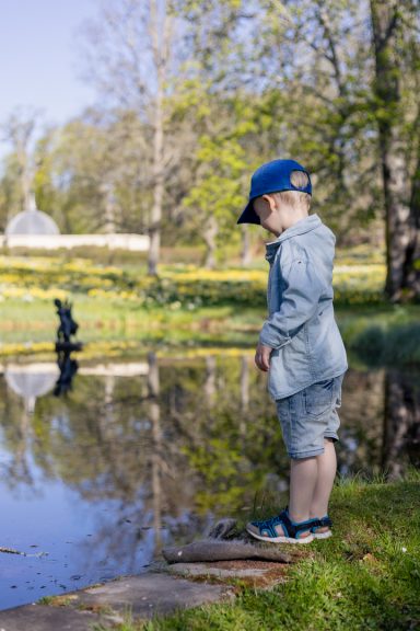 Barn tittar ner i dammen i Adelsnäsparken utanför Åtvidaberg medan påskliljorna blommar i bakgrunden, familjefotograf Anna Esmelöv