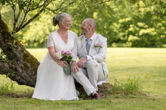 Brudpar sitter på trädgren och tittar varandra kärleksfullt i ögonen efter vigsel utanför Åtvidaberg, fotograferat av Anna Esmelöv