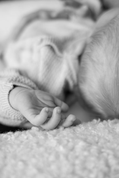 Svartvit dokumentär bild av en bebishand och bebishuvud, fotograferad av Anna Esmelöv